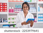 Young hispanic woman pharmacist using touchpad working at pharmacy