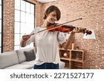 Young beautiful hispanic woman musician smiling confident playing violin at home