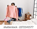 African american woman holding sweater doing laundry at bedroom