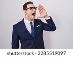 Young hispanic man wearing suit and tie shouting and screaming loud to side with hand on mouth. communication concept. 
