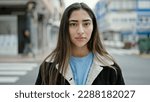 Small photo of Young beautiful hispanic woman standing with serious expression at street