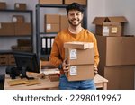 Small photo of Hispanic man with beard working at small business ecommerce holding packages smiling with a happy and cool smile on face. showing teeth.