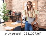 Young blonde woman working at the office holding bike helmet and laptop clueless and confused expression. doubt concept. 