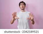 Young hispanic man standing over pink background afraid and terrified with fear expression stop gesture with hands, shouting in shock. panic concept. 