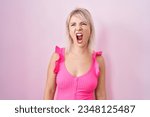 Small photo of Young caucasian woman standing over pink background angry and mad screaming frustrated and furious, shouting with anger. rage and aggressive concept.