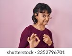 Small photo of Young beautiful woman standing over pink background disgusted expression, displeased and fearful doing disgust face because aversion reaction. with hands raised