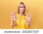 Small photo of Young caucasian woman wearing yellow sweater moving away hands palms showing refusal and denial with afraid and disgusting expression. stop and forbidden.