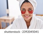 Small photo of Young latin woman having baggy eyes treatment sitting on bed at bedroom