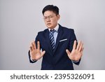 Small photo of Young asian man wearing business suit and tie moving away hands palms showing refusal and denial with afraid and disgusting expression. stop and forbidden.