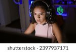 Small photo of Stunning young hispanic woman streamer dominates the gaming landscape, an intimate night of serious gaming in a decked-out room