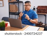 Small photo of Young hispanic man working at the office with laptop disgusted expression, displeased and fearful doing disgust face because aversion reaction. with hands raised