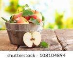 Wooden tub full of freshly harvested red apples with a halved apple on display on a wooden tabletop outdoors with copyspace