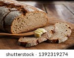 Loaf of sliced rye bread with wooden butter spreader with scoop of butter on an old board viewed low angle on a table with copy space