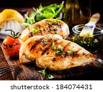Marinated grilled healthy chicken breasts cooked on a summer BBQ and served with fresh herbs and lemon juice on a wooden board, close up view