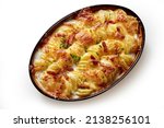 Top view of appetizing gratin with baked sliced potato and crispy bacon pieces baked in oval shaped pan placed on white background