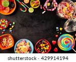 Small photo of Frame of colorful bright assorted candy in bowls and jars, candy canes and rainbow colored spiral lollipops on black with scattered candy hearts and jellybeans around a central copy space on slate