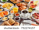 Huge healthy breakfast spread on a table with coffee, orange juice, fruit, muesli, smoked salmon, egg, croissants, meat and cheese