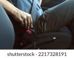Small photo of A man is driving down the road in his car and fastening his seat belt, close-up view of the hand and clasp inside the automobile, safe driving according to the rules of the road.