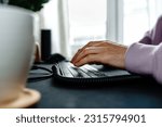 Close up of male hands typing on the computer keyboard while sitting at a desk indoors. no face