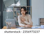 Small photo of An Asian female has a heart attack pain, and tension-sick employee who is feeling heartache while working on a laptop at the workplace at a desk in the office.
