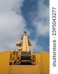 Small photo of Details of a yellow industrial crane against blue cloud sky. Heave duty machinery for construction outdoor.