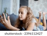 Small photo of A blonde teenage girl is surfing the internet using her phone. Problems that may arise in children due to excessive use of gadgets.