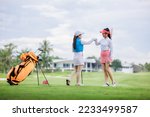 Small photo of two asian women golfers congratulate high-five and happy smiling at golf course, with the golf bag next to them, sport women professional golfer concept