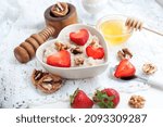 Breakfast with oatmeal with strawberries, honey, walnuts and egg on white background. Breakfast for child. Oatmeal in a white heart-shaped bowl