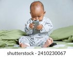 Small photo of The little Asian girl under 1 year old had just woken up and was sitting on the bed playing with the remote.