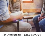 Small photo of A young christian man holding bible and share Jesus story with other two person while sitting on wooden chair in working place against window light. Christian concept background with copy space.