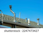 Chimney vents in rows on top of double gable style roof with gray pannels on top of house or home with gradient blue sky. Late in the afternoon sunlight in a suburban part of downtown neighborhood.