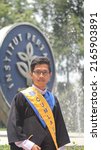 Small photo of BOGOR, INDONESIA - NOVEMBER 9, 2021: Young asian man taking a picture on university graduation day in IPB University campus landmarks "koin IPB". Bogor Agricultural University. Cumlaude predicate.