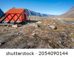 Owl River emergency shelter in remote arctic wilderness with a backpack in front of it . Sunny day in Akshayuk Pass valley, Auyuittuq National Park, Baffin Island, Nunavut, Canada.