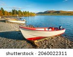 White wooden boats on lake shore with mountains in the distance. Beautiful sunny day of autumn in remote Swedish arctic. Lulealven lake, Stora Sjofallet national park, Kebnats, Sweden