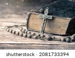 Detail studio shot of very old, vintage Holy Bible with lots of ornaments on the cover and yellow pages and old rosary on vintage wooden desk Christianity concept. Time of prayer.