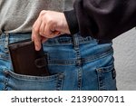 Small photo of The hand of a thief pulling a purse wallet out of someone's pocket. Blue jeans pocket with pouch. Closeup concept of theft, crime, dishonesty.