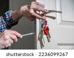 Small photo of Door lock installation, repair, or replacement service. Door hardware installer locksmith working with open white door indoor. Keychain close-up, new dwelling or moving house.