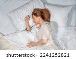 Woman sleeping in bed at home. Deep restful sleep. Lady with long brown hair wearing a nightgown. High Angle View girl lying in a nightie on clean white bed linen with cozy blanket.