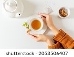 Composition with female hands holding a cup of tea, teapot, cinnamon and tea bag on white background. Flat lay, top view. Slow morning concept.