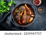Modern style traditional braised slow cooked lamb shank in red wine sauce with shallots and carrots offered as top view in a design stewpot 