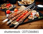 Small photo of Traditional Turk Adana kebap on shashlik skewer with barbecue vegetable, flatbread and yogurt as close-up on a rustic metal tray