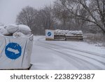 Small photo of empty roadblock on the road. concrete slabs, sandbags and anti-tank hedgehogs restrict traffic. military structures on a winter road. blizzard and ice on the road at the patrol post.