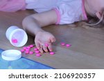 Small photo of Unconscious little child (girl) with pink pills on the floor at home. Danger of medicament intoxication.