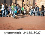 Small photo of Gubbio Umbria, Italy-May 15 2011; Couple at front of crowd of people gathered in European town square as sun lowers and shadows lengthen in late afternoon.