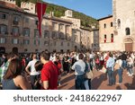 Small photo of Gubbio Umbria, Italy-May 15 2011; Crowd facing away gather in European town square as sun lowers and shadows lengthen in late afternoon.