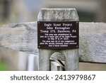 Small photo of Doylestown, PA, USA, 10.23.22 - A sign attached to a wooden fence post giving credit to the Eagle Scounts.