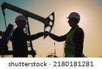 Small photo of Oil pump. Engineers handshake. Corporate contract. People in helmets work at oil pump. Business contract handshake silhouette. Deposit of minerals. Working engineers teamwork in field at the oil pump