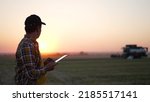 Small photo of Agriculture. Agronomist senior stands with tablet in wheat field, harvests in background. combine harvests wheat on farmer's field. Agronomist senior with tablet. man in agriculture