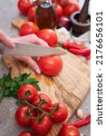 Small photo of woman making notch on a tomato on wooden cutting board on grey kitchen concrete or stone table