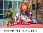 Small photo of blonde Argentinian adult woman with curlers, at home sitting watching camera mixing and shuffling tarot cards to start therapeutic tarot consultation, copy space